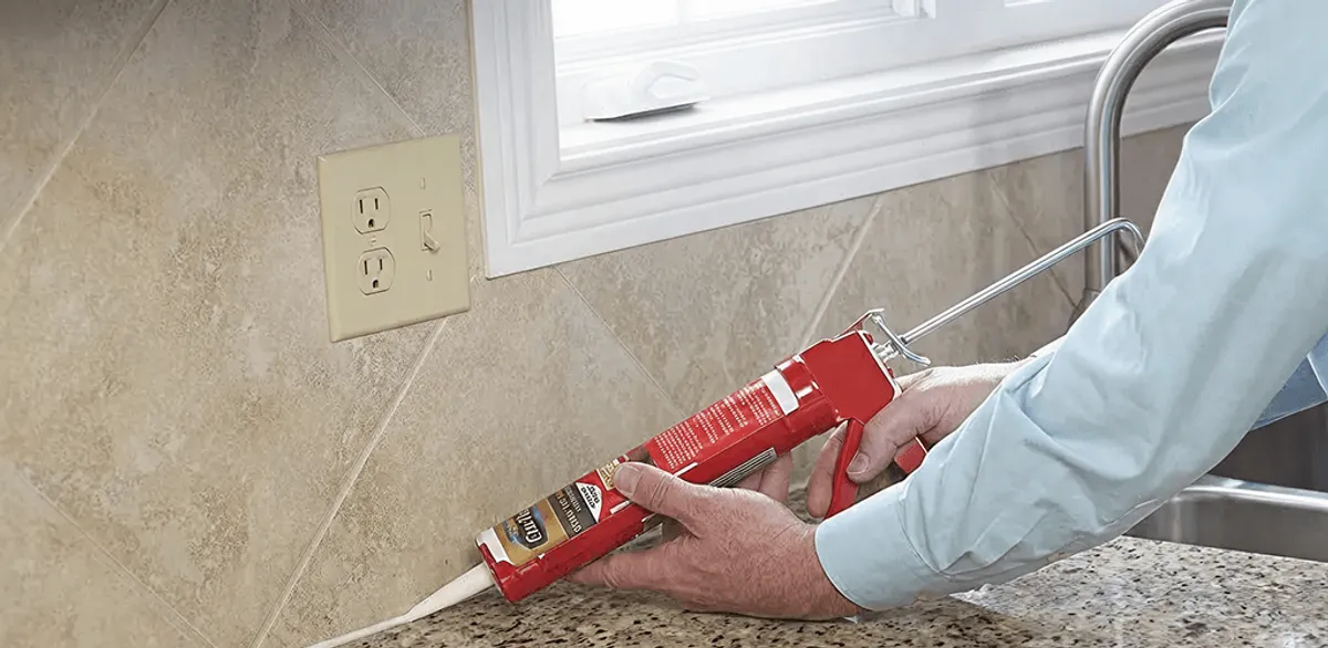 Handyman applying caulk along a kitchen backsplash and countertop seam in Des Moines, IA