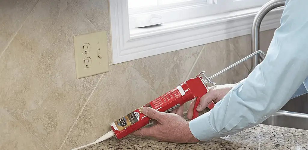Handyman applying caulk along a kitchen backsplash and countertop seam in Des Moines, IA