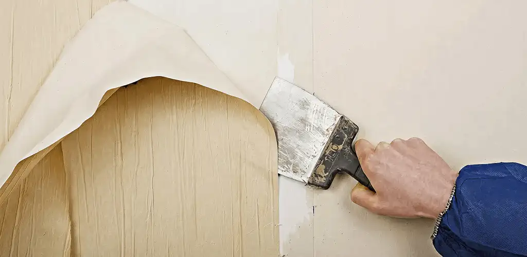 Handyman removing wallpaper with a scraper for wall preparation in Des Moines, IA