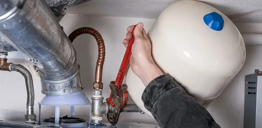 Water heater repair technician tightening plumbing connections near a tank unit in Des Moines, IA